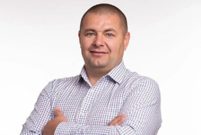 Чоловік у світлій картатій сорочці зі схрещеними руками на білому тлі