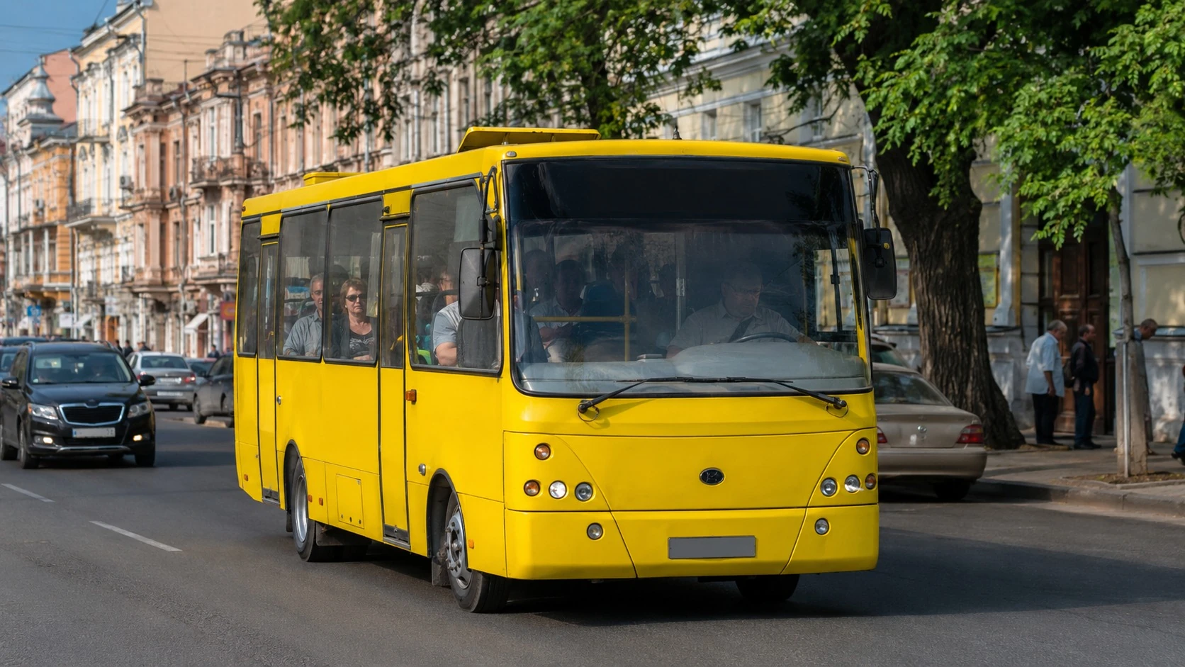 Жовта маршрутка їде вулицею міста з пасажирами у вікнах