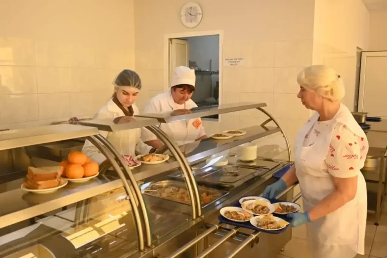 Кухарки в білій формі роздають гарячі страви за вітриною шкільної їдальні