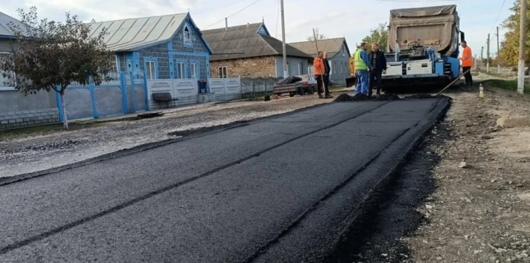 Свіжий асфальт на сільській вулиці біля хат, робітників і асфальтоукладача
