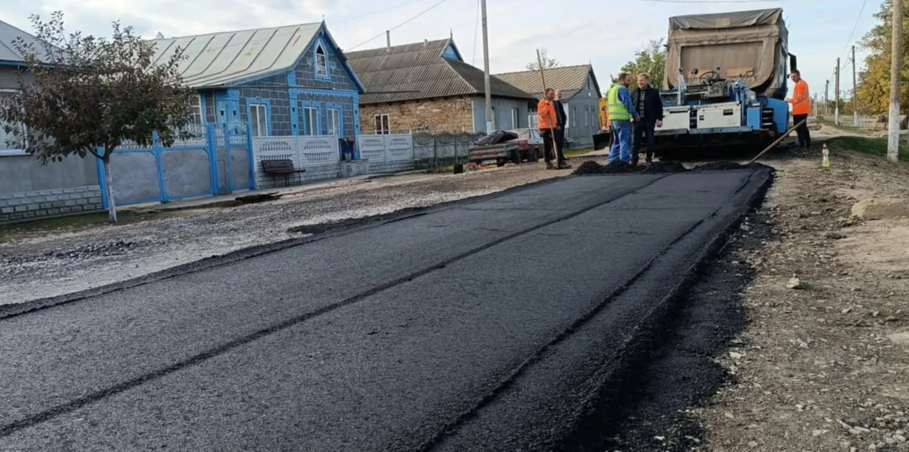 Свіжий асфальт на сільській вулиці біля хат, робітників і асфальтоукладача