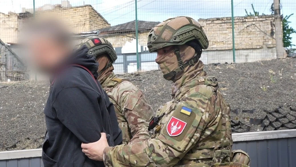 Українські військові в камуфляжі супроводжують чоловіка з розмитим обличчям біля руїн