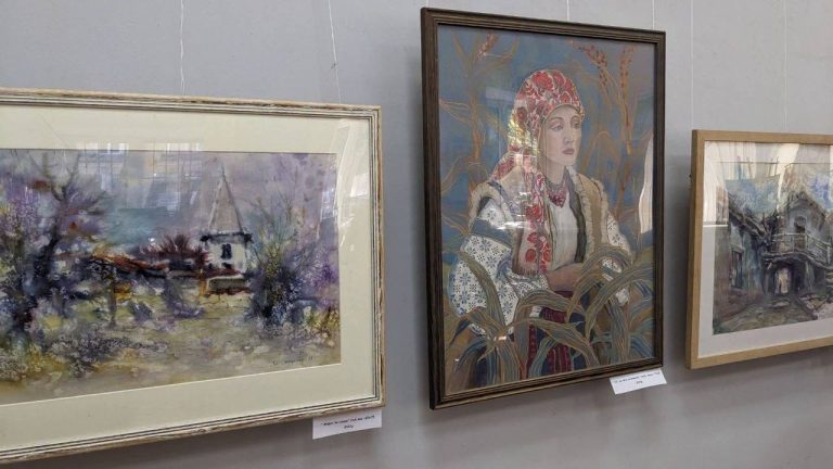 Три картини на стіні виставки: пейзаж, портрет дівчини в народному вбранні та хата